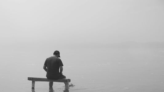 Man sitting alone on bench in foggy lake in black and white, disconnected and mentally clouded