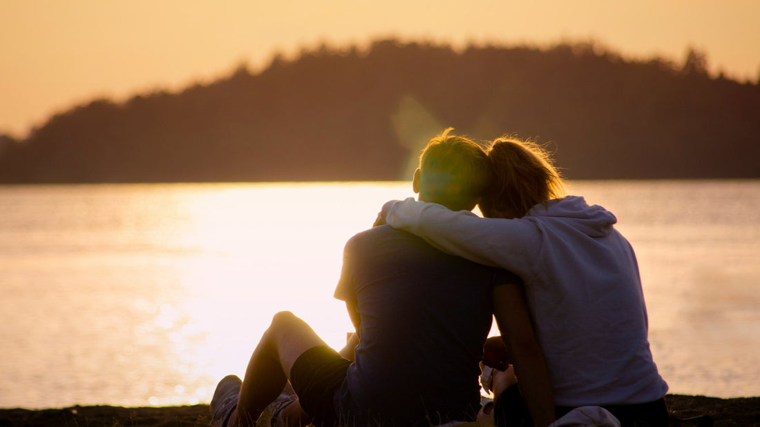 Couple sitting together by a lake at sunset, enjoying a peaceful moment of rest and doing the bare minimum