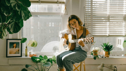 Woman playing guitar in a bright plant-filled room, morning affirmations for anxious minds work by redirecting attention before anxiety sets the tone for the day