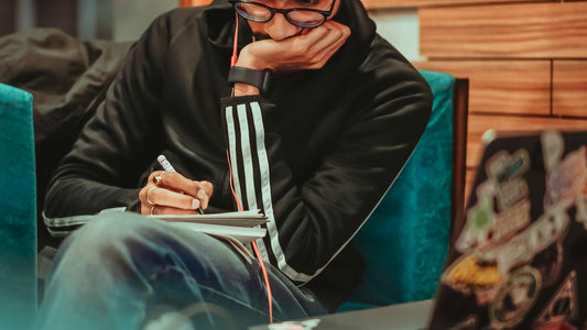 Man with headphones writing in a notebook with coffee nearby, starting the task without waiting to feel motivated