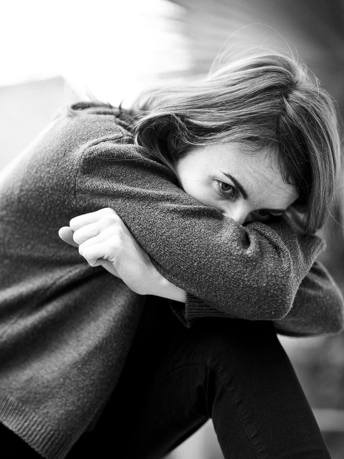 Black and white portrait of a young woman hunched over with face buried in her hands, showing physical signs of burnout