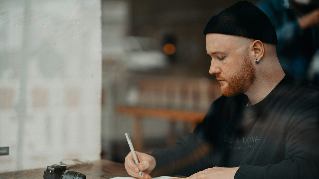 Person writing in a journal at a café table, starting a new journaling habit