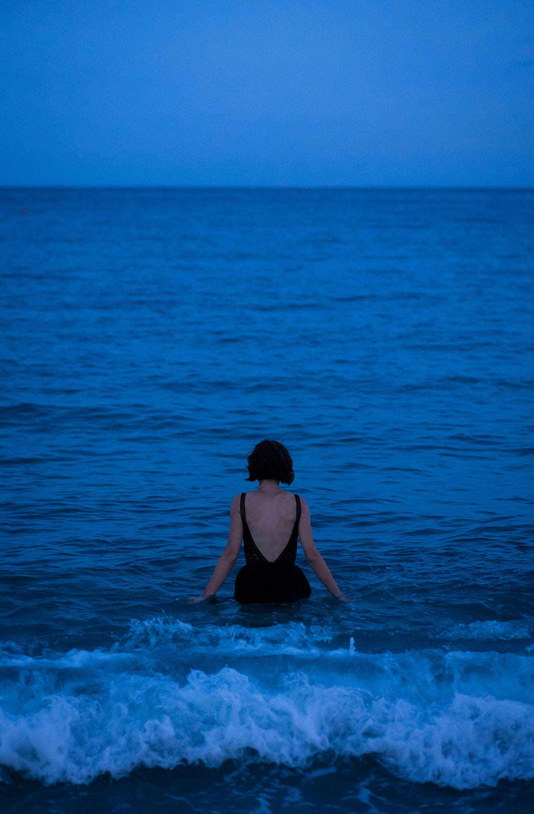Woman wading alone into a dark blue evening sea, back to camera, what to write in a journal starts with what is already present
