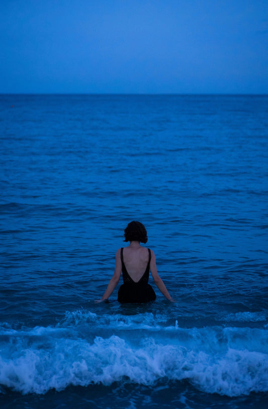 Woman wading alone into a dark blue evening sea, back to camera, what to write in a journal starts with what is already present