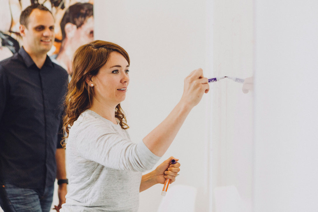 Woman writing goals on a whiteboard in a bright office, setting objectives and planning outcomes