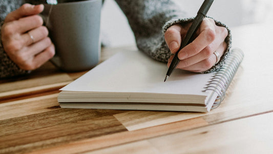 Woman writing calmly in a notebook beside a mug, tracking her mood each morning