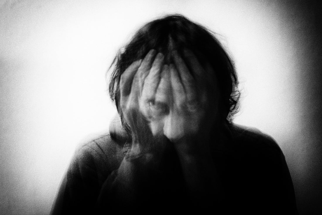 Black and white motion-blurred portrait of a person covering their face, representing perfectionism-related overwhelm