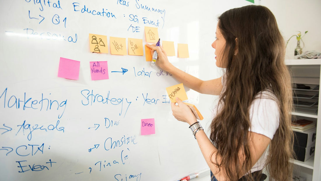 Woman writing ideas on a whiteboard covered in sticky notes, focused and mid-thought