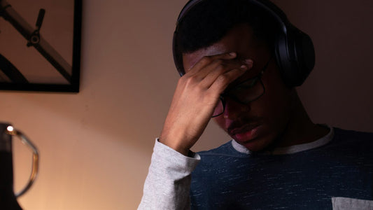A young man at a home desk looking stressed and overwhelmed while doomscrolling on his laptop late at night