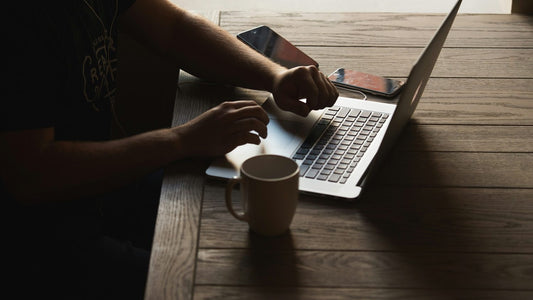 Man with hands on laptop keyboard, staring blankly at the screen in dim late-night lighting