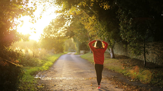 Woman in a red jacket jogging down a sunlit tree-lined country lane at sunrise
