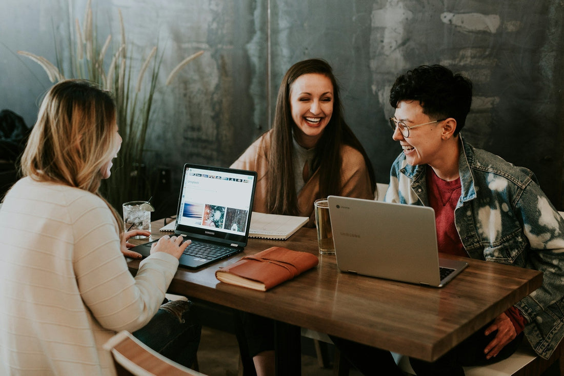 Three people laughing together at a café table, the social setting where the spotlight effect makes you feel watched