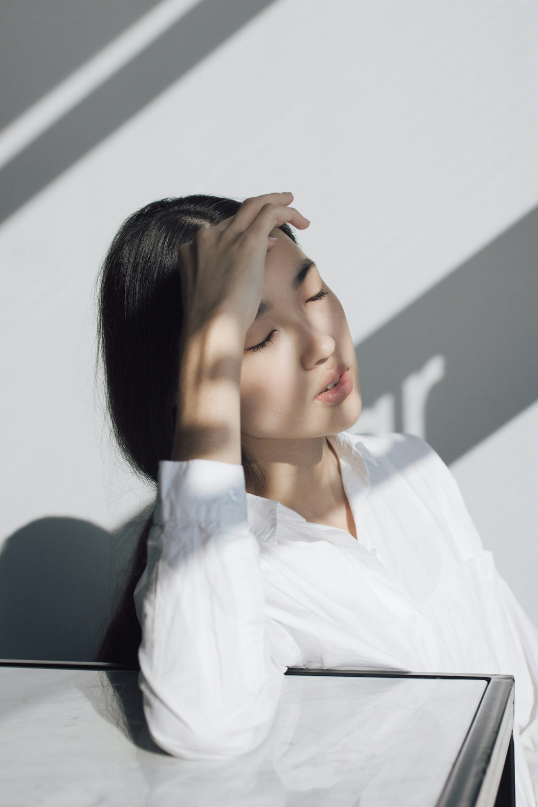 Woman with eyes closed and a hand to her head in soft daylight, calming her nervous system with vagus nerve exercises