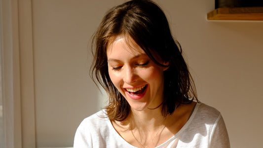 Woman pausing with a smile in warm morning light, a quiet moment of gratitude at home