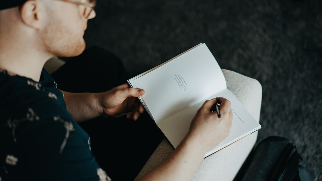 Man in glasses writing in an open notebook on his lap, starting a daily journaling habit