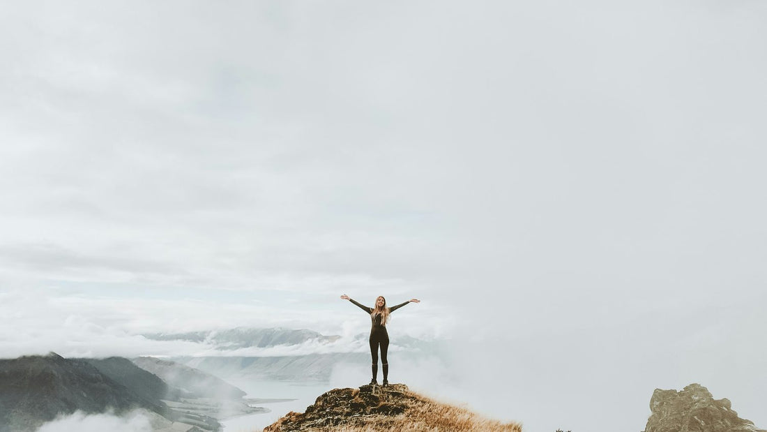 Woman on a mountain summit with arms spread wide, aspirational energy for vision board quotes