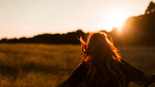 Woman in a golden sunset field with eyes closed, calm and rested, learning how to wake up early without strain