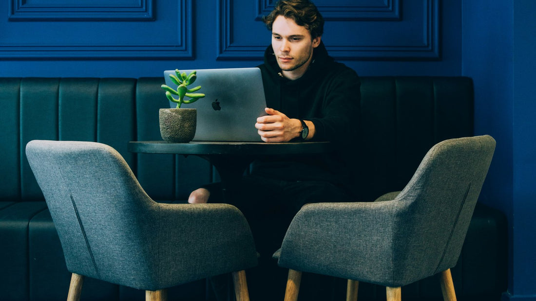 Person sitting alone at a table in a blue room, deep in thought, weighed down by perfectionism