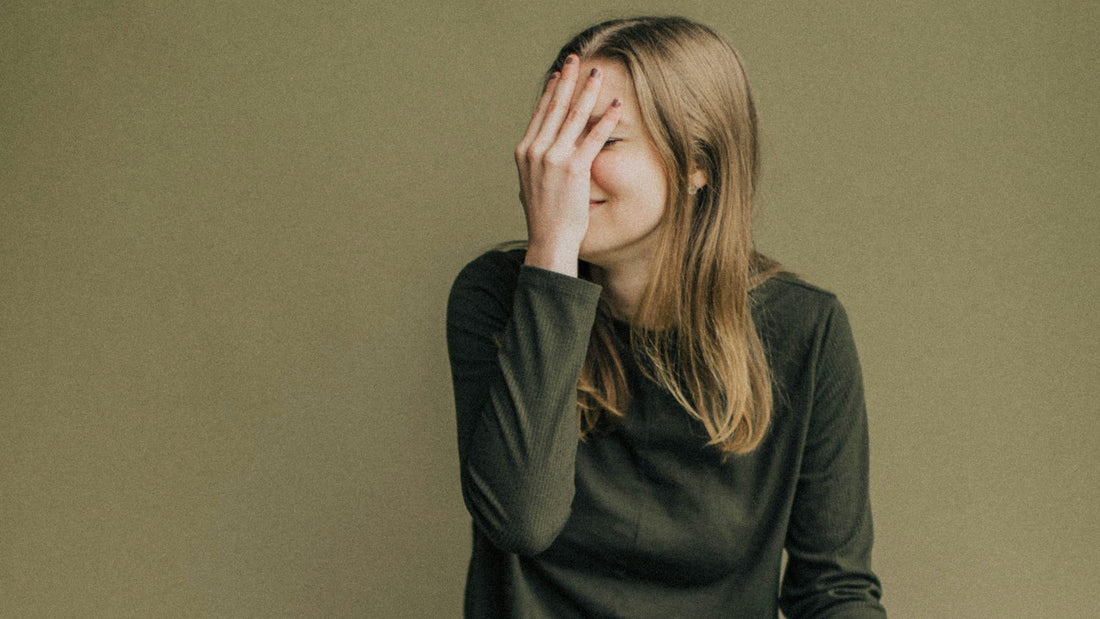 Woman sitting quietly with her hand over her face, processing a sense of self-worth tied to her achievements, separating identity from achievement