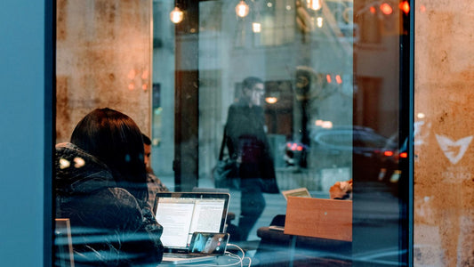 Person working through a laptop screen reflection in a cafe window, quietly focused mid-morning
