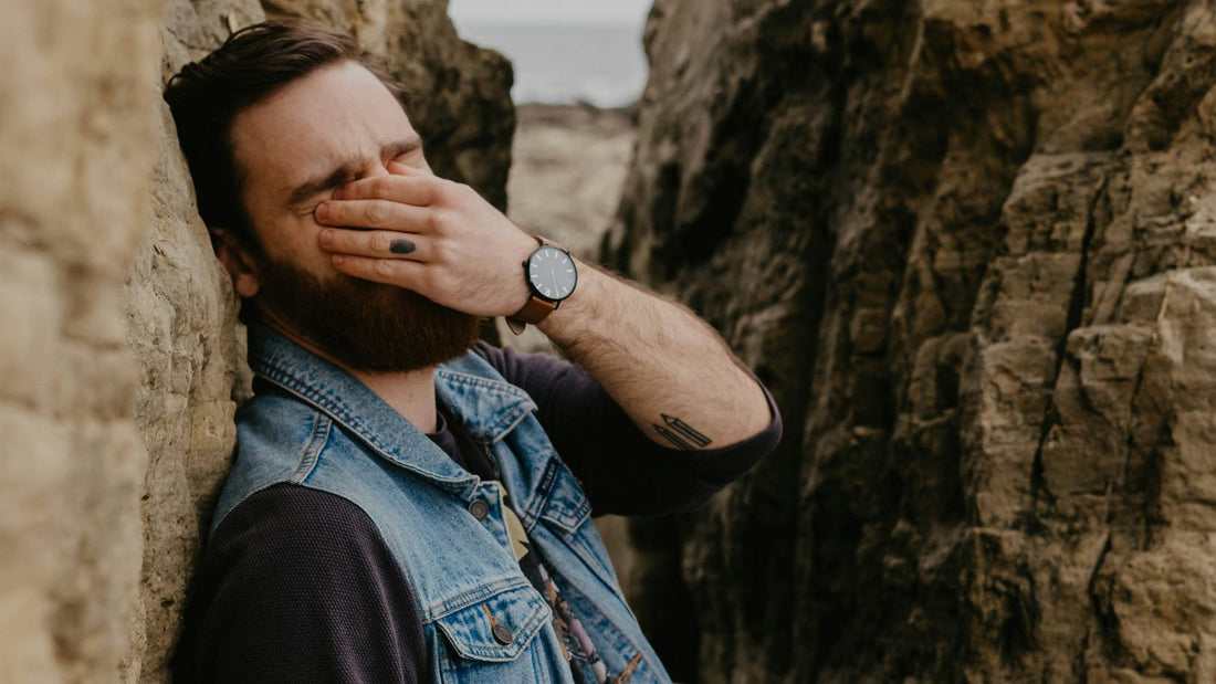 Man leaning against rocks with hand covering his face, discouraged after abandoning a resolution