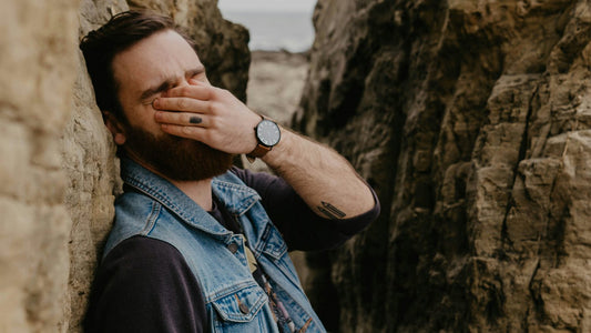 Man leaning against rocks with his hand over his face, overwhelmed and depleted, restore balance mindful living