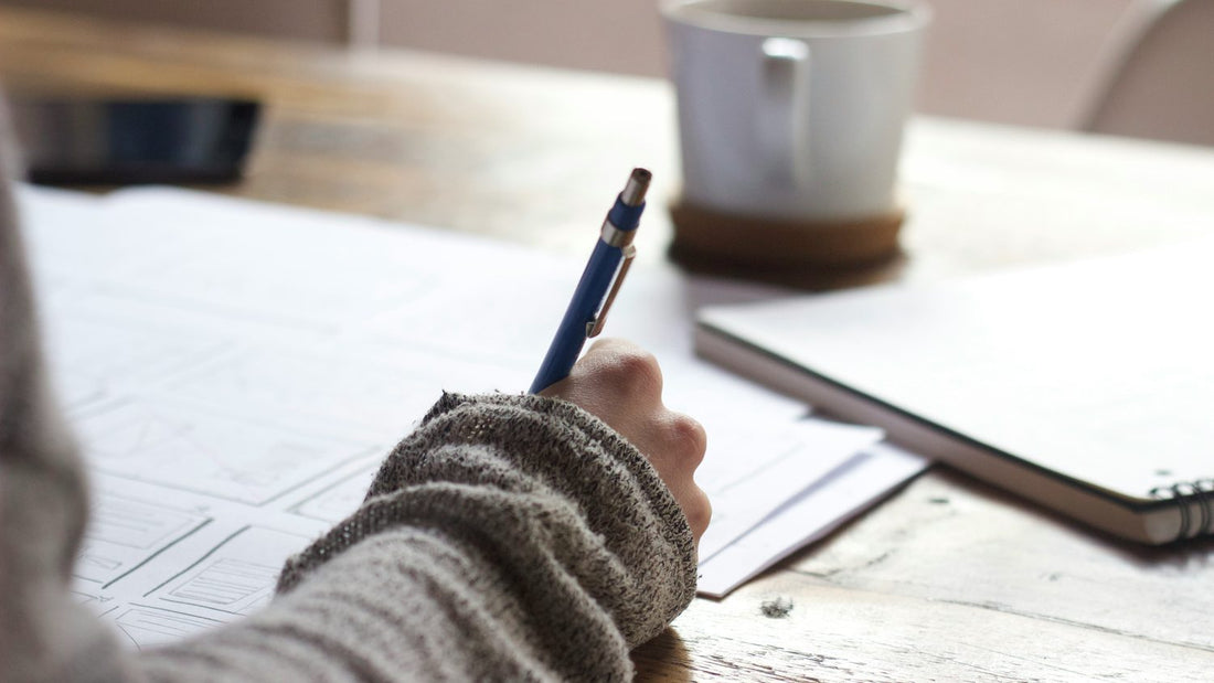 Person writing in a notebook beside an open laptop, calm and focused, building a habit routine
