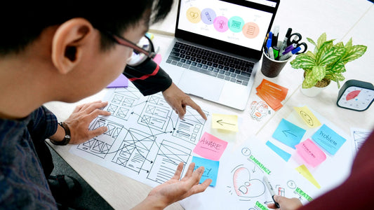Overhead view of a man reviewing wireframes and sticky notes, turning feedback into a revised plan