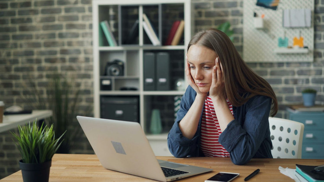Woman with hands on temples looking stressed and overworked at her laptop