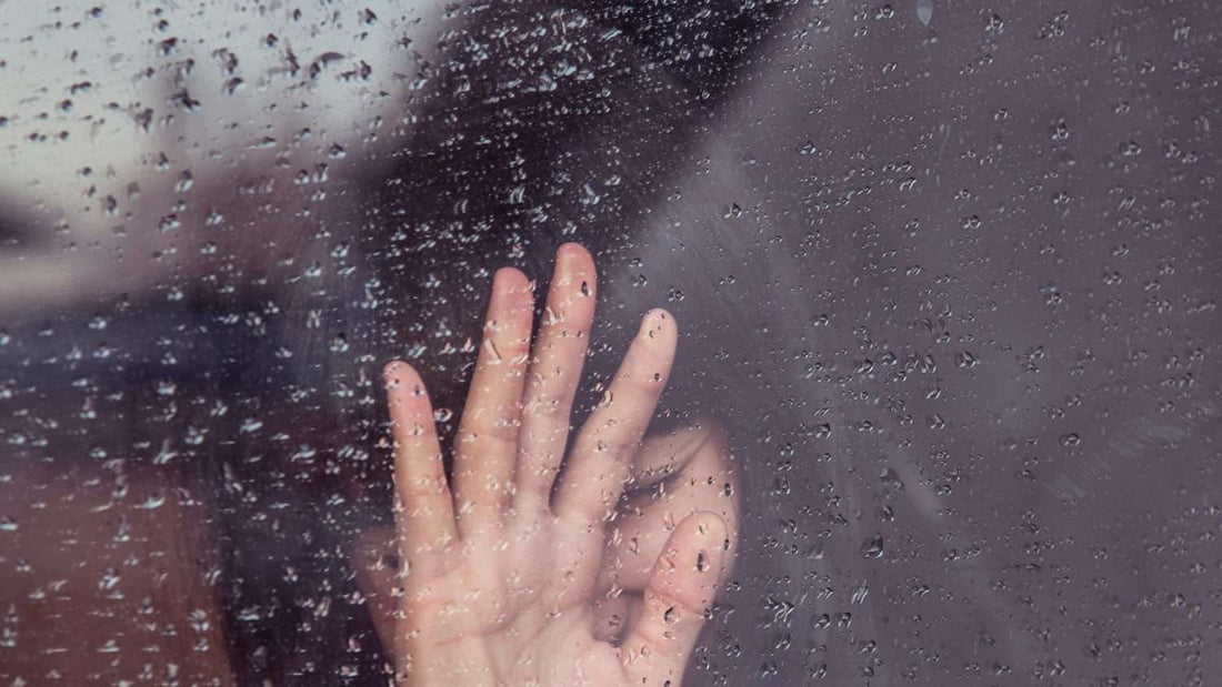 Woman with hand pressed to rainy window, reflecting the shutting-down feeling of overwhelm