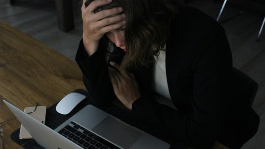Woman with head in hands at a dark desk, overwhelmed and unable to focus