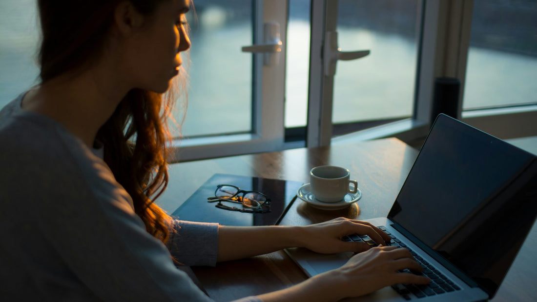 Woman typing on laptop late at desk, surrounded by tasks, looking drained